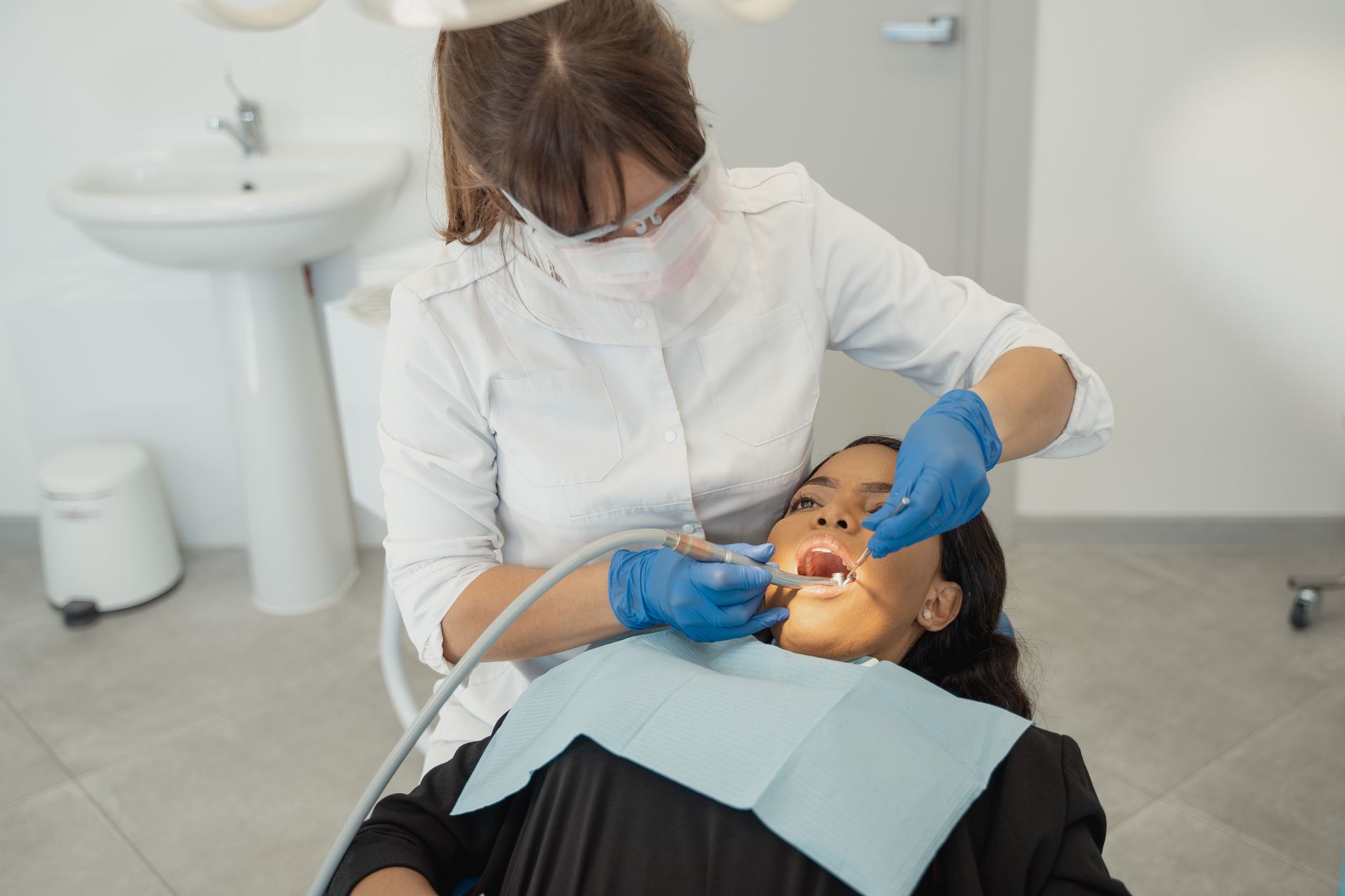 A dentist wearing a facemask examines a patient's teeth